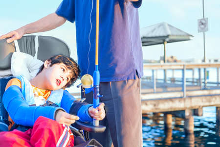 Caucasian father helping disabled ten year old son in wheelchair fish off pierの写真素材