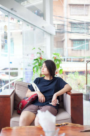 Beautiful biracial teen  girl sitting in hotel lobby looking out window with bored or tired expressionの写真素材