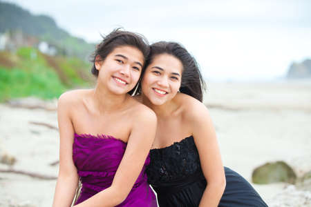Two beautiful biracial Asian Caucasian teen girls in elegant dresses smiling together on the beach with ocean in the backgroundの写真素材