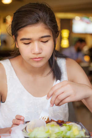 Biracial teen girl smiling, eating shrimp with chopsticks in restaurantの写真素材