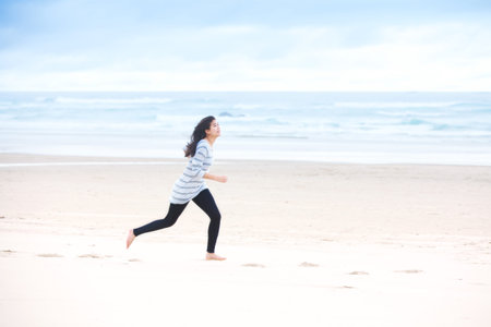 Young biracial teen girl running on beach by oceanの写真素材