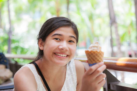 Biracial teen girl, holding ice cream cone, smilingの写真素材