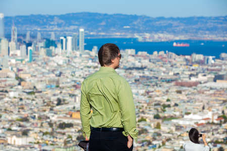 Tall Caucasian man standing on top of high point of Twin peaks looking down over the city of San Franciscoの写真素材