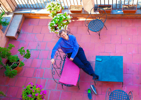 Handsome Caucasian man in early fifties relaxing on Italian patio covered in red terracotta tiles, smiling and looking up towards cameraの写真素材