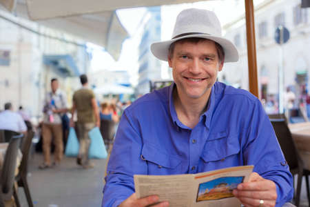 Handsome Caucasian man in early fifties sitting at outdoor cafe in Italy or Europe, ready to order from menu.の写真素材