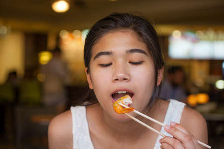 Biracial teen girl eating jumbo shrimp at restaurant, mouth open ready to eatの写真素材