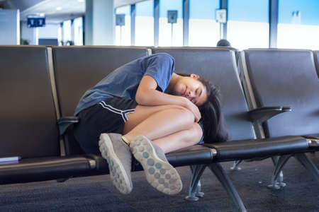 Biracial Asian Caucasian teenage girl sleeping on airport bench, tiredの写真素材
