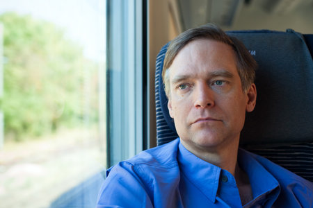 Caucasian man in forties wearing blue shirt sitting on commuter train