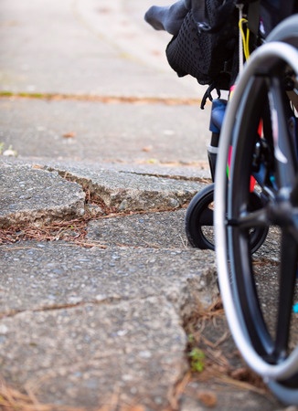 Wheelchair wheel stuck against large cracks in broken sidewalk pavementの写真素材