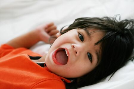 Handsome little disabled boy wearing orange shirt lying down smiling at cameraの写真素材