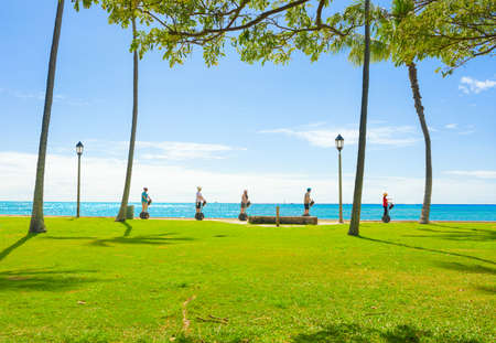 Group of five toursits riding self balancing scooters along the ocean walking path in Waikiki, Honolulu, Hawaii on bright sunny dayのeditorial素材