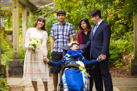 Newly married bride and groom posing together with family outdoors under vine covered pergola next...