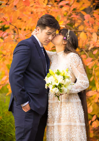 Biracial newly married couple kissing outdoors by bright orange autumn leavesの写真素材