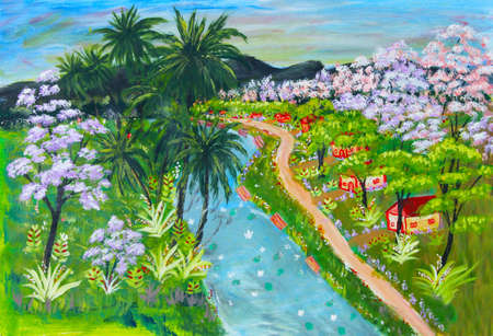 Small rural village huts and homes along a flowing river in a tropical country with coconut trees and flowering trees in full bloomの写真素材