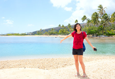 Young woman standing on quiet beach by a calm bay in  Oahu, Hawaiiの写真素材