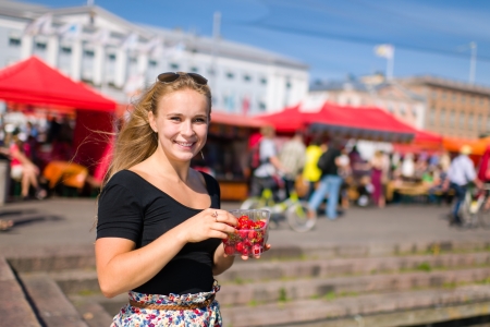 Beautiful girl in the Helsinki market square and she eat strawberries, market stalls on the backgroundの写真素材