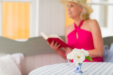 Lady reads a book on the veranda, reposeful atmosphere, vertical format, narrow focus on flower, lady looks outsideの写真素材