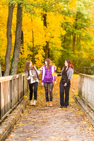 Three sisters walking on bridge and they have a fun together on autumnal parkの写真素材