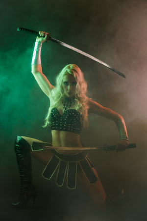 Performer woman wearing sexy costume and holding a samurai sword, grey smoky backgroundの写真素材
