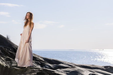 Beautiful young woman wearing white dress, scandinavian shore and sea on backgroundの写真素材