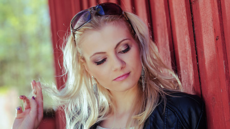 Close up, fashionable beautiful young blond wearing a leather jacket and leans against the red wallの写真素材