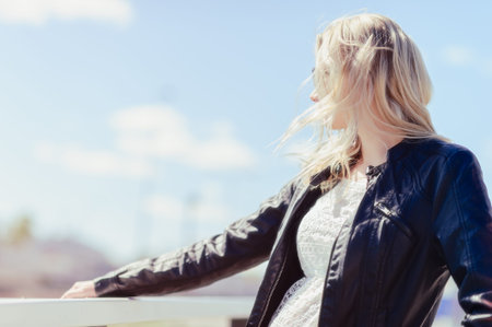 Fashionable beautiful young blond wearing a leather jacket, warm sunny day