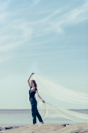 Beautiful young woman and white garment, sunny day on a rocky shoreの写真素材