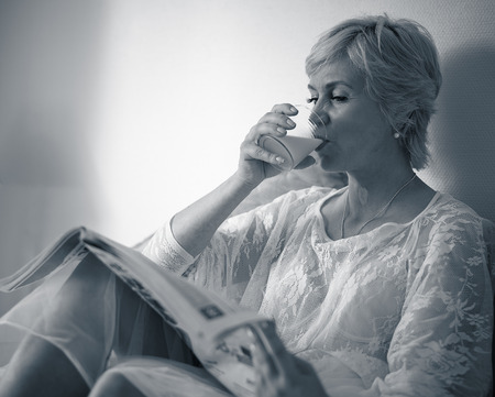 The morning, mature woman reads the newspaper in the bed and drinks juiceの写真素材