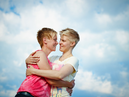 Two women hugging in the afternoon sunlight, cloudy sky on backgroundの写真素材