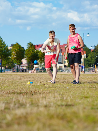 Two women play petanque in the park in the afternoon sunlight, city on backgroundの写真素材