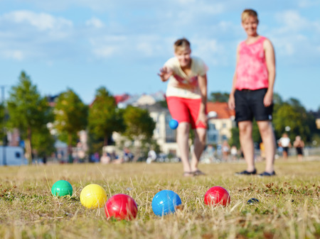 Two women play petanque in the park in the afternoon sunlight, city on backgroundの写真素材