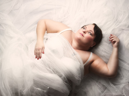 Beautiful plus size woman lying on the bed and looks towards to light.の写真素材
