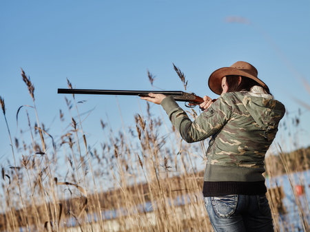 Waterfowl hunting, female hunter use the shotgun, reeds and blue sky on backgroundの写真素材