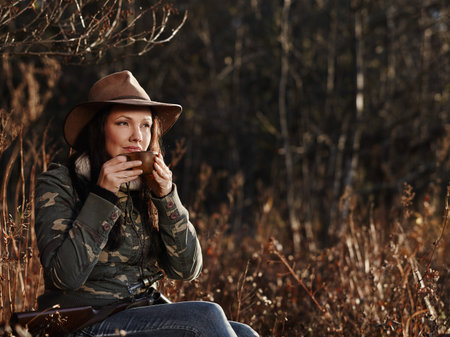 Waterfowl hunting, the female hunter having a coffee break, autumnal bushes on backgroundの写真素材