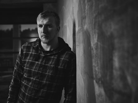 Handsome young man wearing a checked shirt and he lean against the the concrete wall - black and...