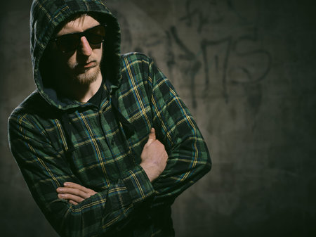 Handsome young man wearing  a checked shirt and a sunglasses, concrete wall - cross processed image