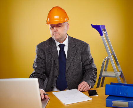 Working male engineer in office, he wearing a white shirt and tie and coat, head he wears a orange hard hatの写真素材