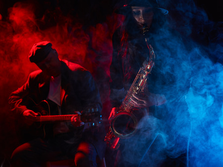 Saxophonist, beautiful young woman, smoky stage and guitarist on backgroundの写真素材