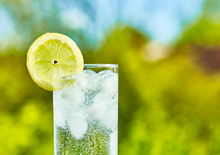 Sparkling water and lemon slice on glass with an ice, sunny day - narrow focus on middle of the glassの写真素材