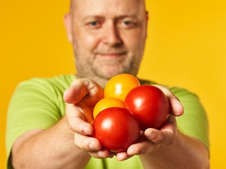 Middle-aged man and fresh ripe tomatoes on hand - yellow backgroundの写真素材