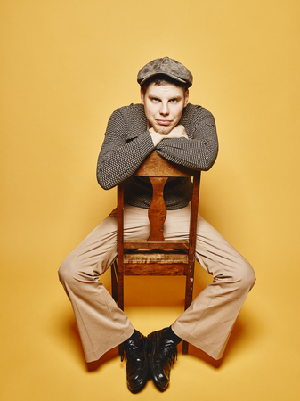 Expressive man sits on the chair and 70's look theme, yellow backgroundの写真素材