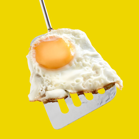 Fried egg, whole egg yolk on metallic spatula, yellow backgroundの写真素材