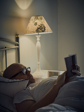 Middle aged man reading Bible on bedの写真素材