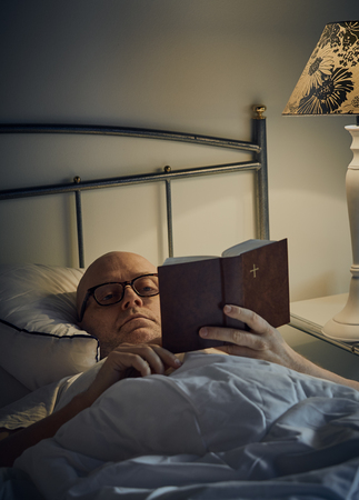 Middle aged man reading Bible on bedの写真素材