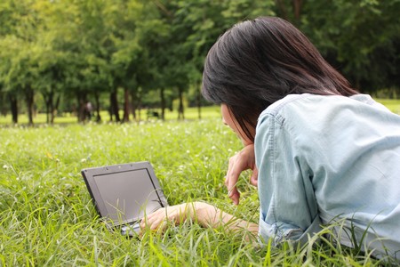 A smiling young girl with laptop outdoors in the parkの写真素材