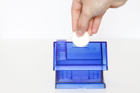 House Blue Money Box on White Background with woman hand with coinの写真素材