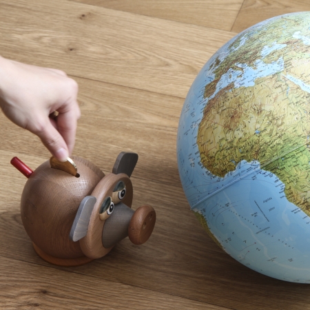 Pig money box with hand with coin and globe. Pig is staring at globe.の写真素材