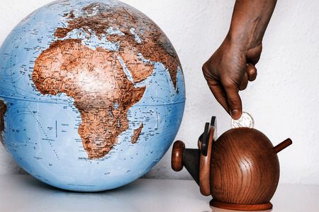 Pig money box with hand with coin and globe. Pig is staring at globe.の写真素材