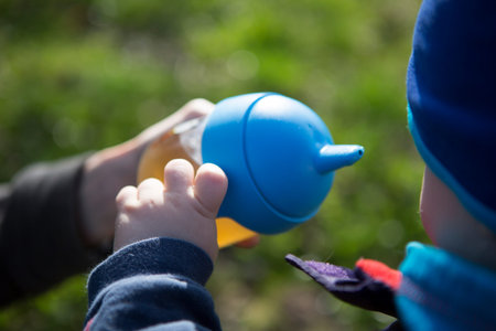little child drinking water from blue plastic bottle with hat