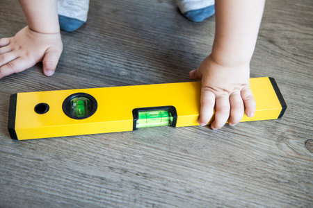 spirit level in young boy hand - child with waterlevel, wood floor